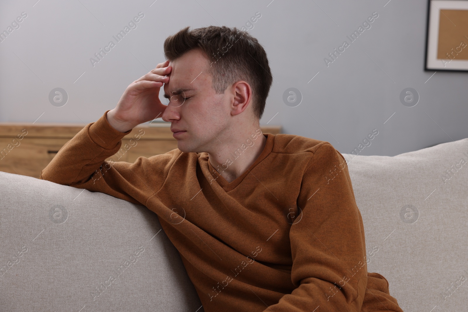 Photo of Sad man suffering from headache on sofa indoors