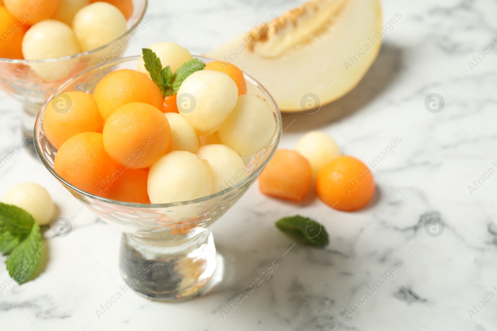 Photo of Melon balls and mint on white marble table, closeup. Space for text
