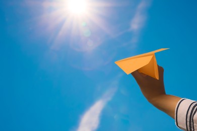 Image of Woman holding orange paper plane against blue sky, closeup. Space for text