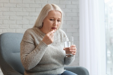 Mature woman taking pill against headaches at home