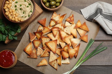 Photo of Delicious pita chips with hummus, olives and sauce on wooden table, flat lay