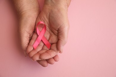 Photo of Senior woman holding pink ribbon on color background, top view with space for text. Breast cancer awareness