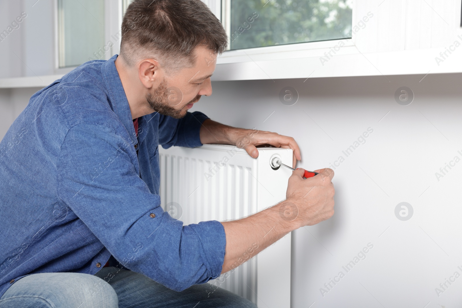 Photo of Man with screwdriver fixing radiator at home