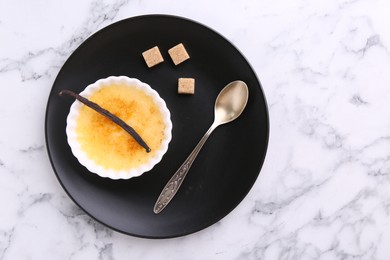 Photo of Delicious creme brulee in bowl, vanilla pod, sugar cubes and spoon on white marble table, top view. Space for text