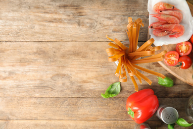 Uncooked buckwheat noodles and fresh ingredients on wooden table, flat lay. Space for text