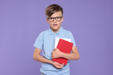 Photo of Cute schoolboy in glasses holding books on violet background