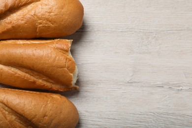 Photo of Whole and broken tasty baguettes on white wooden table, flat lay. Space for text