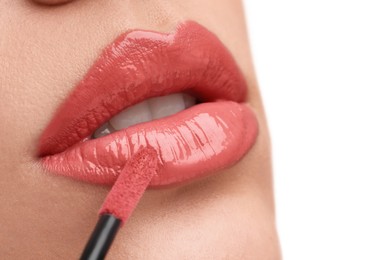 Woman applying lip gloss on white background, closeup