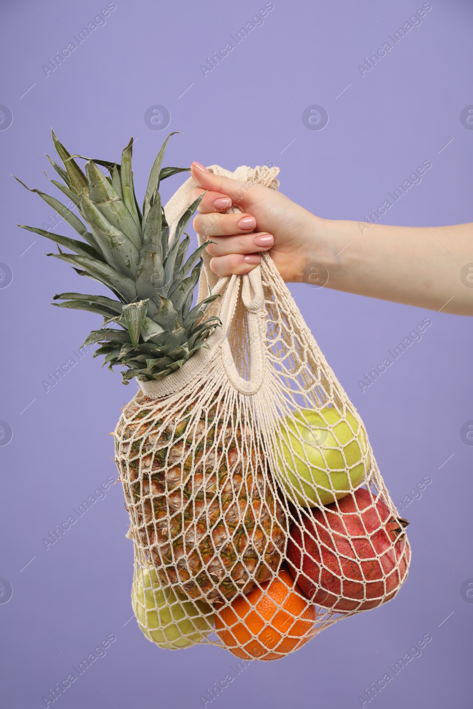 Photo of Woman with string bag of fresh fruits on violet background, closeup