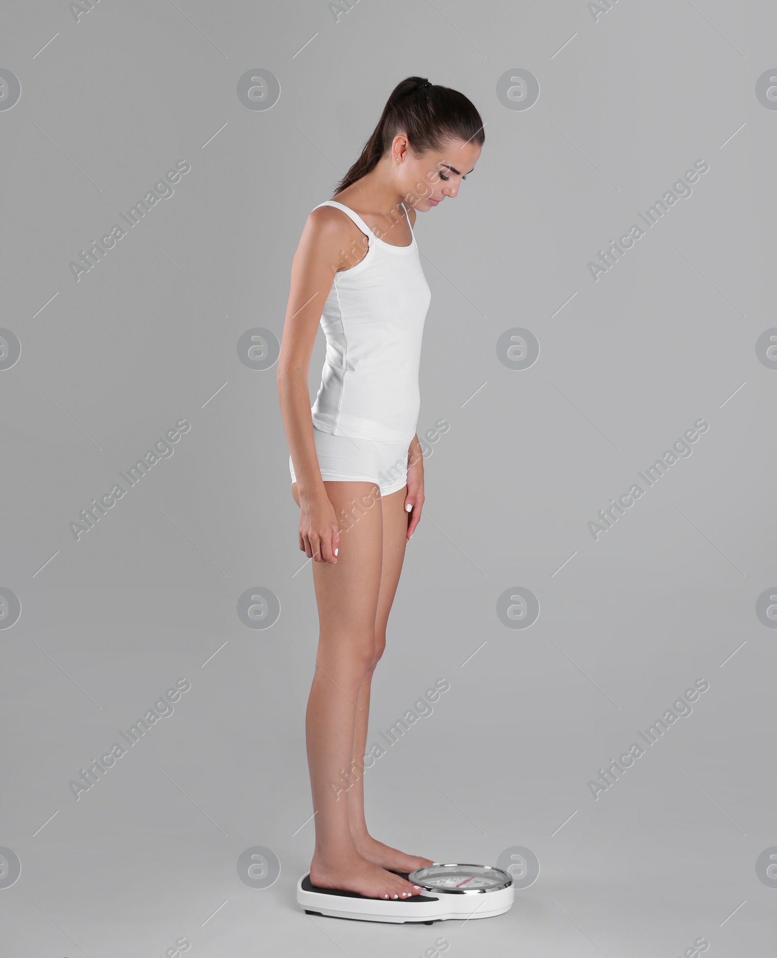 Photo of Young woman measuring her weight using scales on color background. Weight loss motivation