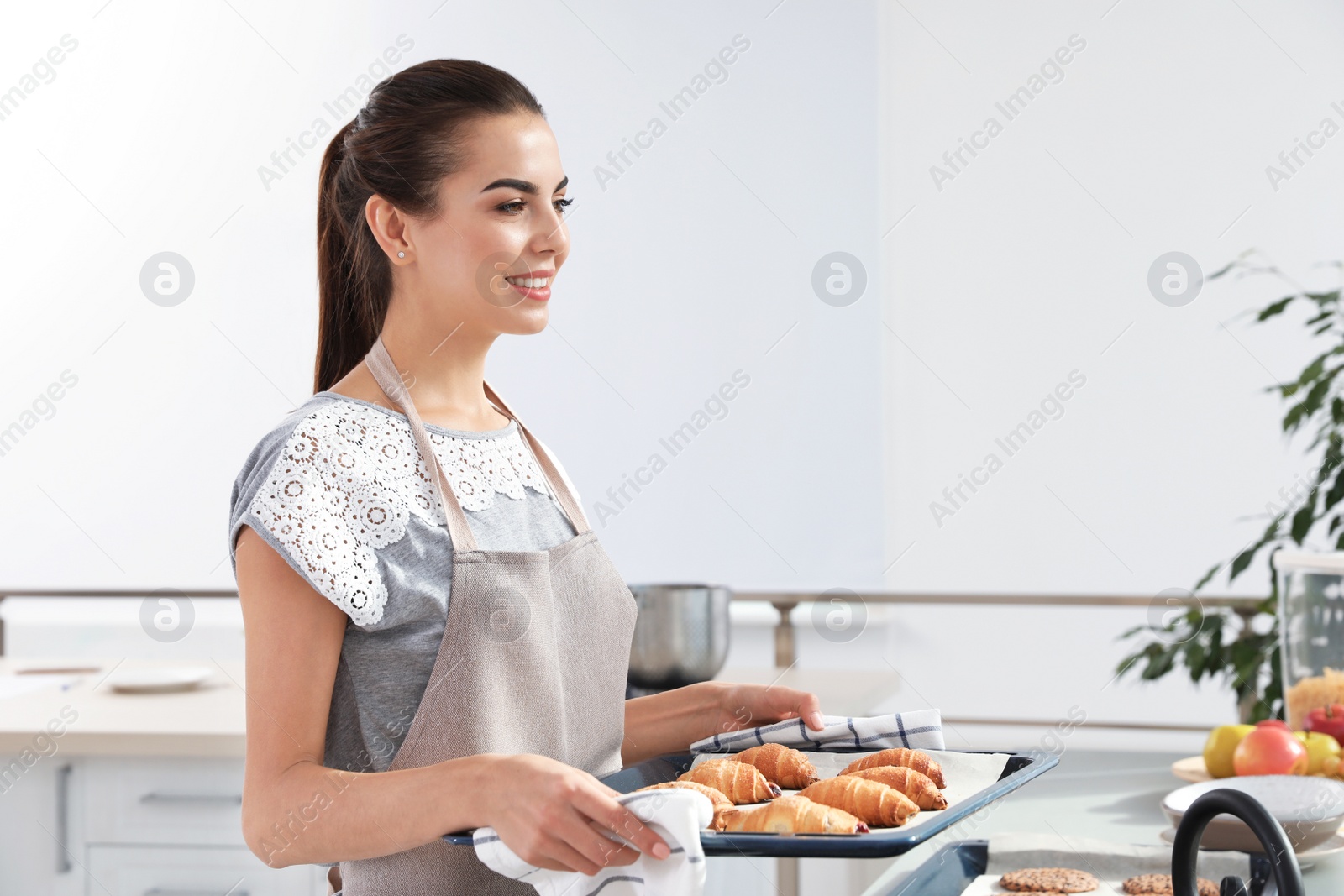 Photo of Young woman holding oven sheet with homemade croissants in kitchen, space for text