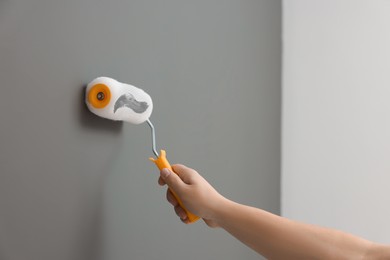 Photo of Worker using roller to paint wall with grey dye indoors, closeup