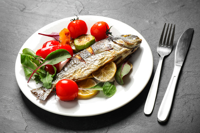 Photo of Delicious roasted fish with lemon and vegetables on dark grey table