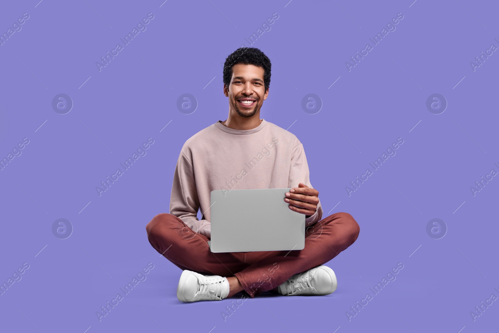 Photo of Happy man with laptop sitting on purple background