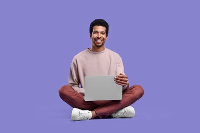 Photo of Happy man with laptop sitting on purple background