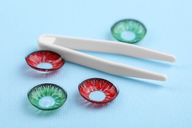 Photo of Different color contact lenses and tweezers on light blue background