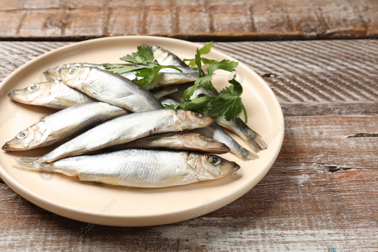 Photo of Fresh raw sprats and parsley on wooden table, closeup