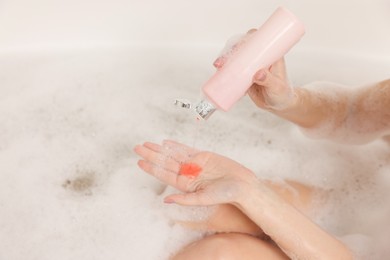 Woman pouring shower gel onto hand in bath indoors, closeup. Space for text