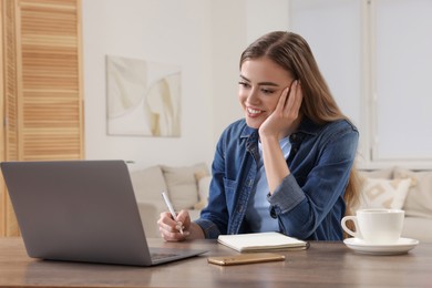 Happy woman with notebook using laptop at wooden table in room