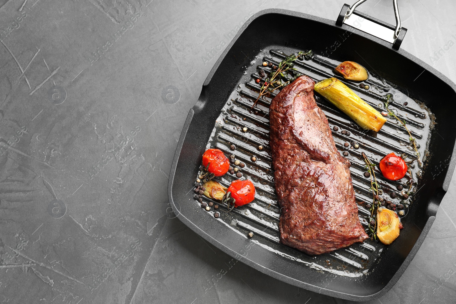 Photo of Delicious grilled beef meat and vegetables in pan on grey table, top view. Space for text