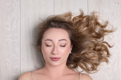 Photo of Portrait of beautiful woman with closed eyes on wooden floor, top view