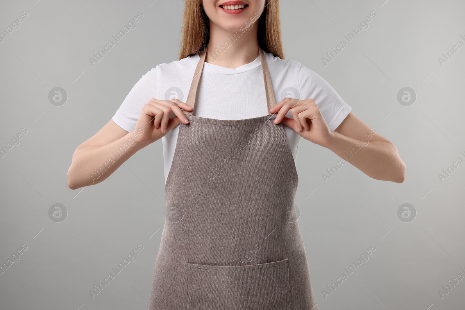 Photo of Woman wearing kitchen apron on grey background, closeup. Mockup for design