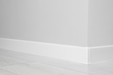 White plinth with connector on laminated floor near wall indoors, closeup