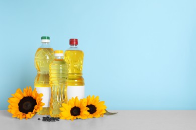 Photo of Bottles of cooking oil, sunflowers and seeds on white table, space for text