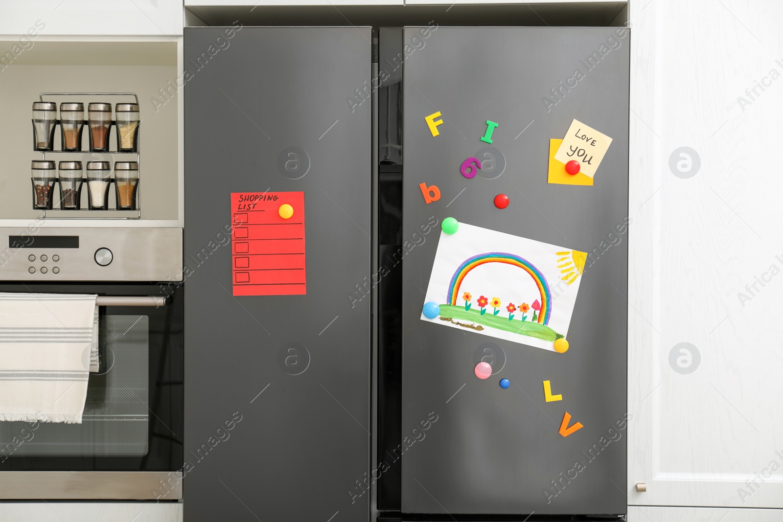 Photo of Modern refrigerator with child's drawing, notes and magnets in kitchen