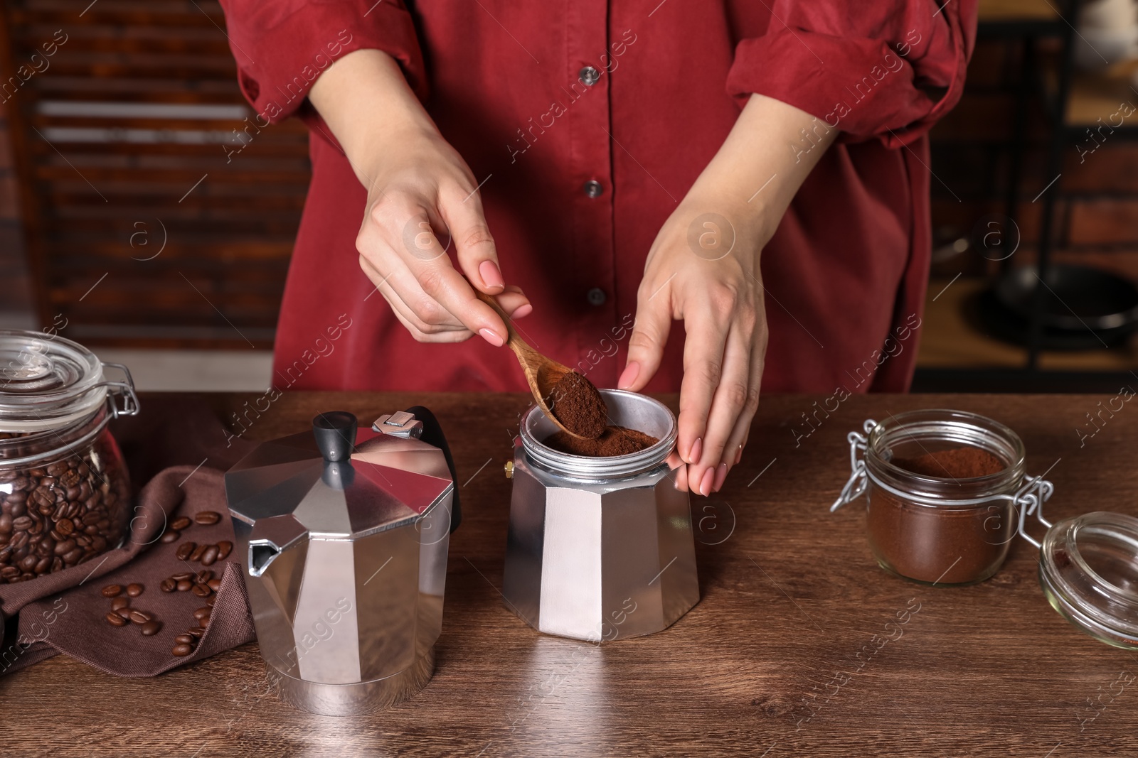 Photo of Woman putting ground coffee into moka pot at wooden table, closeup