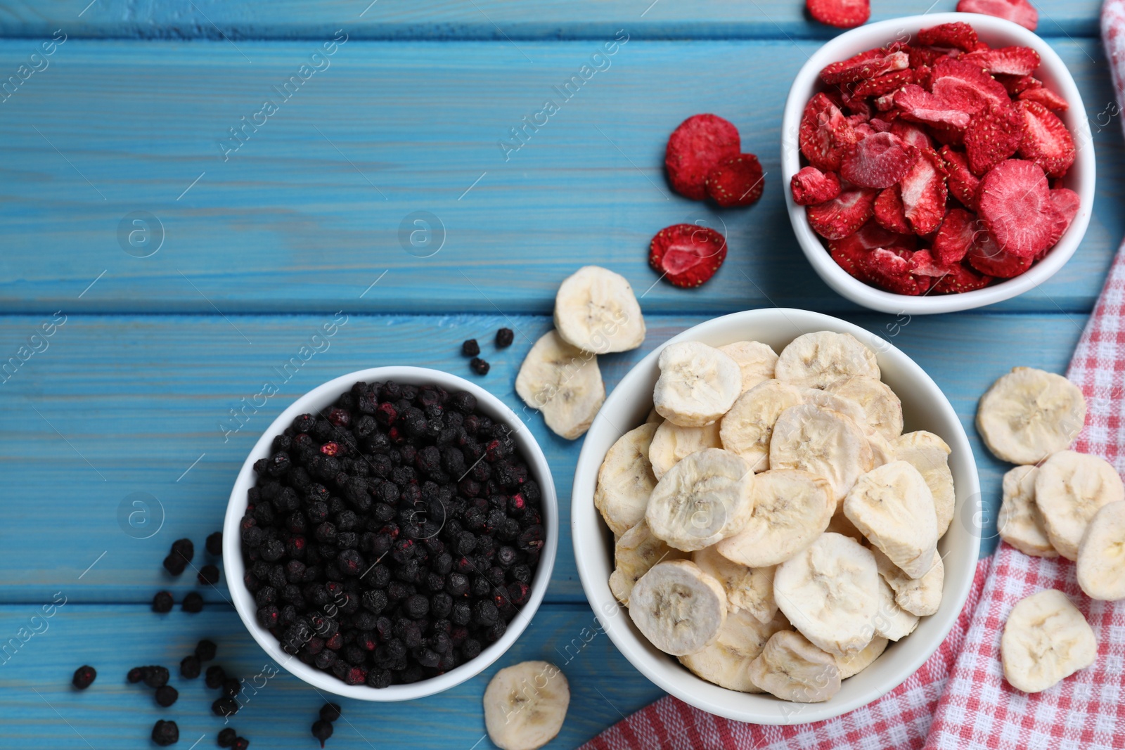 Photo of Bowls and dried fruits on turquoise wooden table, flat lay. Space for text