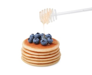 Pouring honey onto delicious pancakes with blueberries on white background