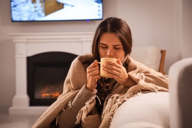 Photo of Young woman drinking from cup near fireplace at home
