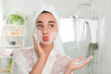 Photo of Beautiful young woman applying cleansing foam onto face in bathroom. Skin care cosmetic