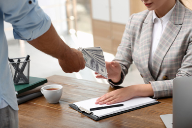 Photo of Man giving bribe money to woman at table, closeup