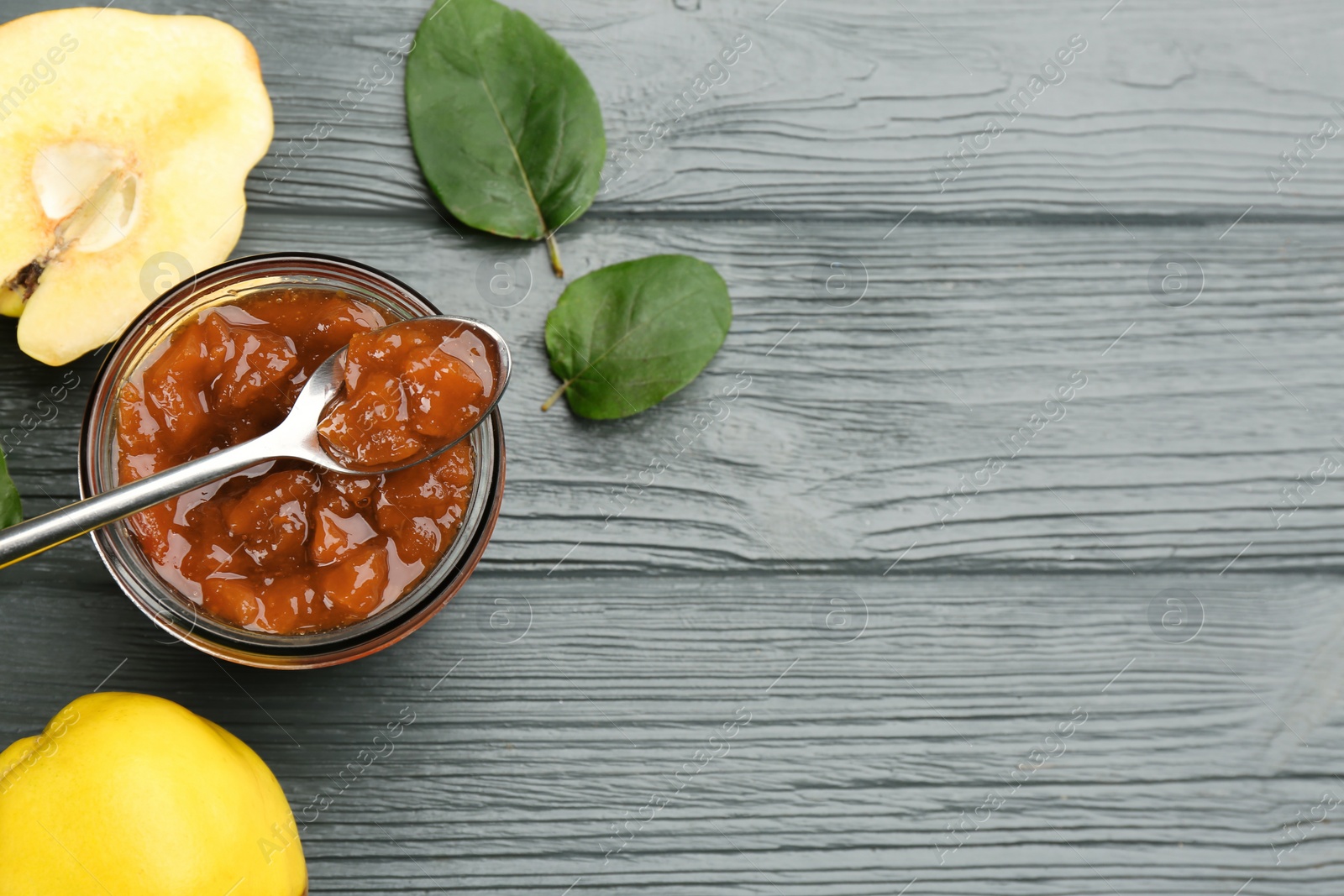 Photo of Delicious quince jam, fruits and leaves on grey wooden table, flat lay. Space for text