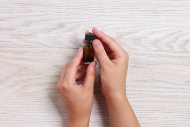 Woman with bottle of essential oil on wooden background, top view