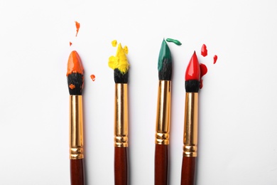 Photo of Brushes with colorful paints on white background, flat lay