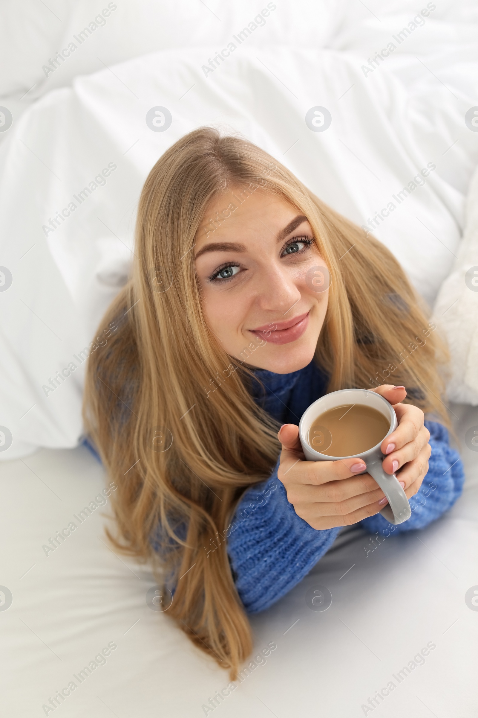 Photo of Beautiful young woman with cup lying in bed at home. Winter atmosphere