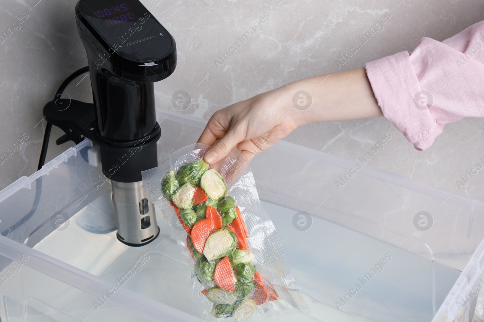 Photo of Woman putting vacuum packed vegetables into box with thermal immersion circulator, closeup. Sous vide cooking