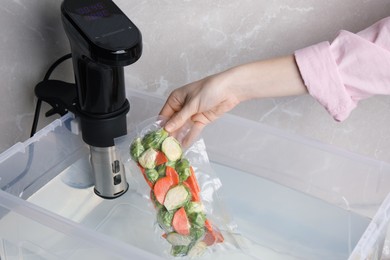 Woman putting vacuum packed vegetables into box with thermal immersion circulator, closeup. Sous vide cooking