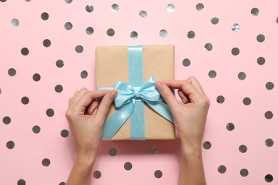 Photo of Woman decorating Christmas gift on pink background with silver glitter, top view