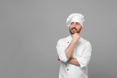 Smiling mature chef on grey background, space for text