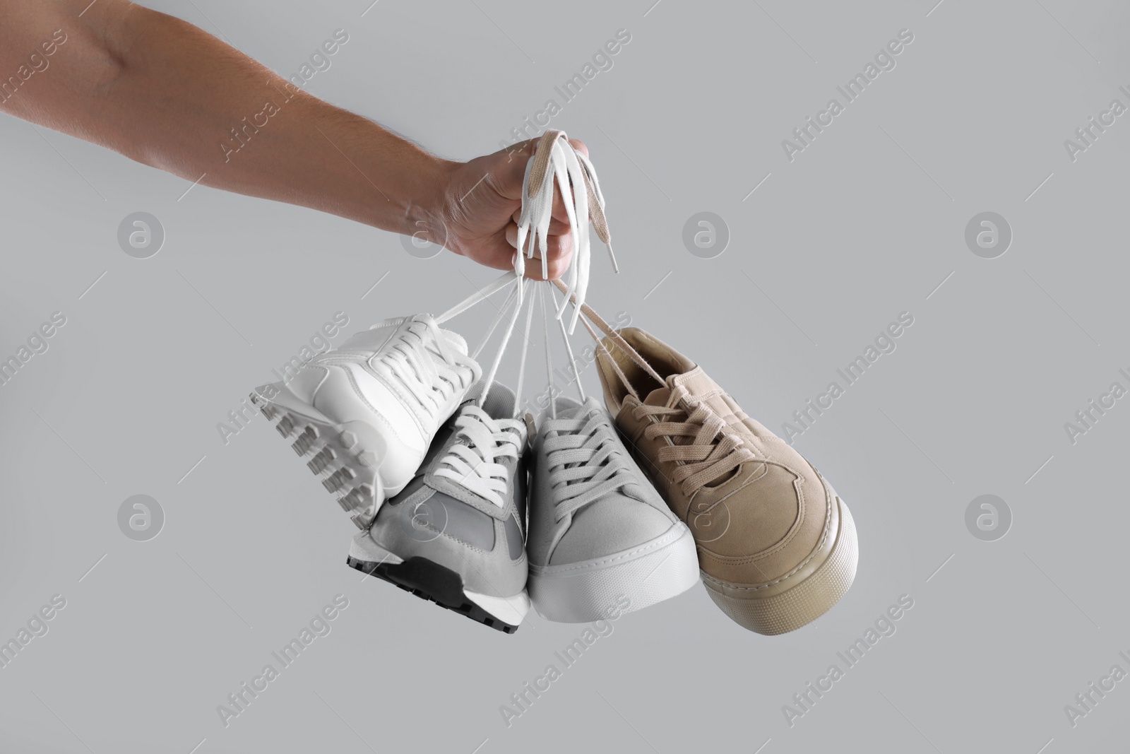 Photo of Man holding different sneakers on light grey background, closeup