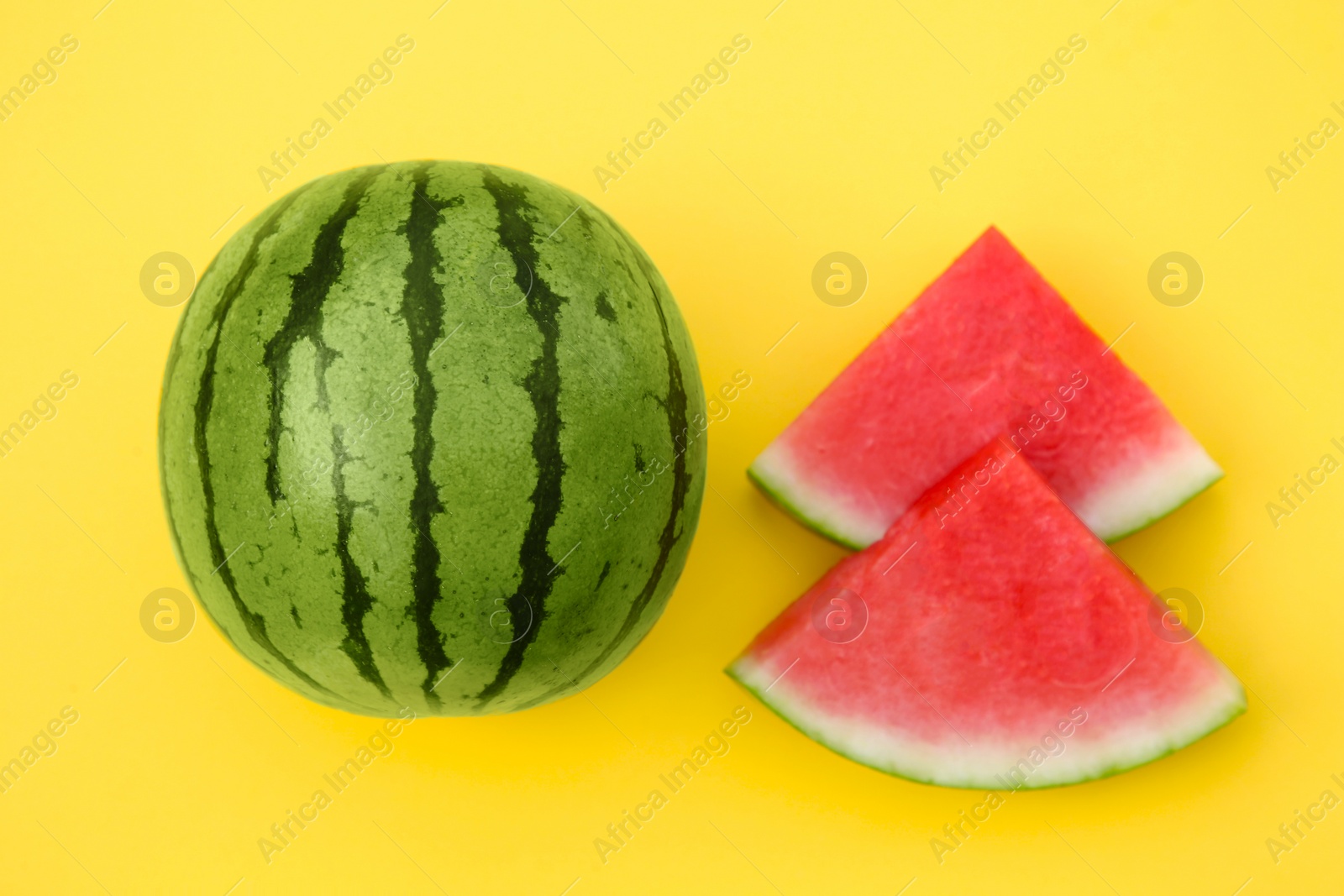 Photo of Delicious cut and whole ripe watermelons on yellow background, flat lay