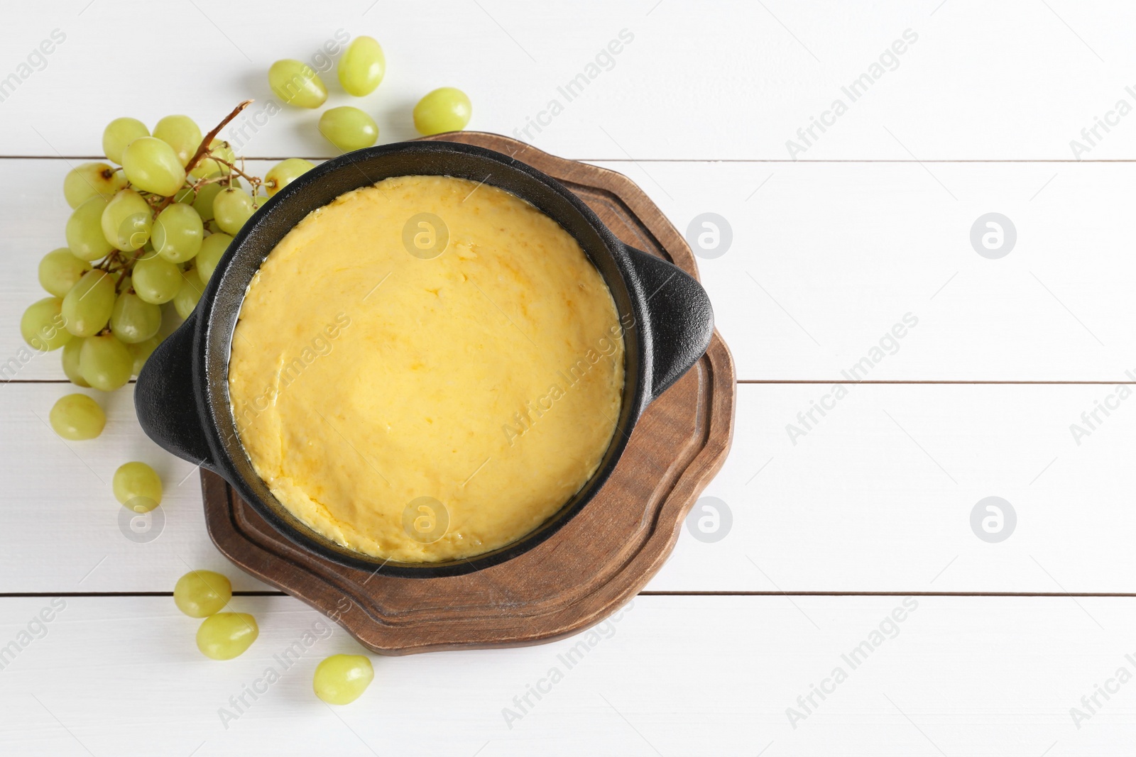 Photo of Fondue with tasty melted cheese and grapes on white wooden table, flat lay. Space for text