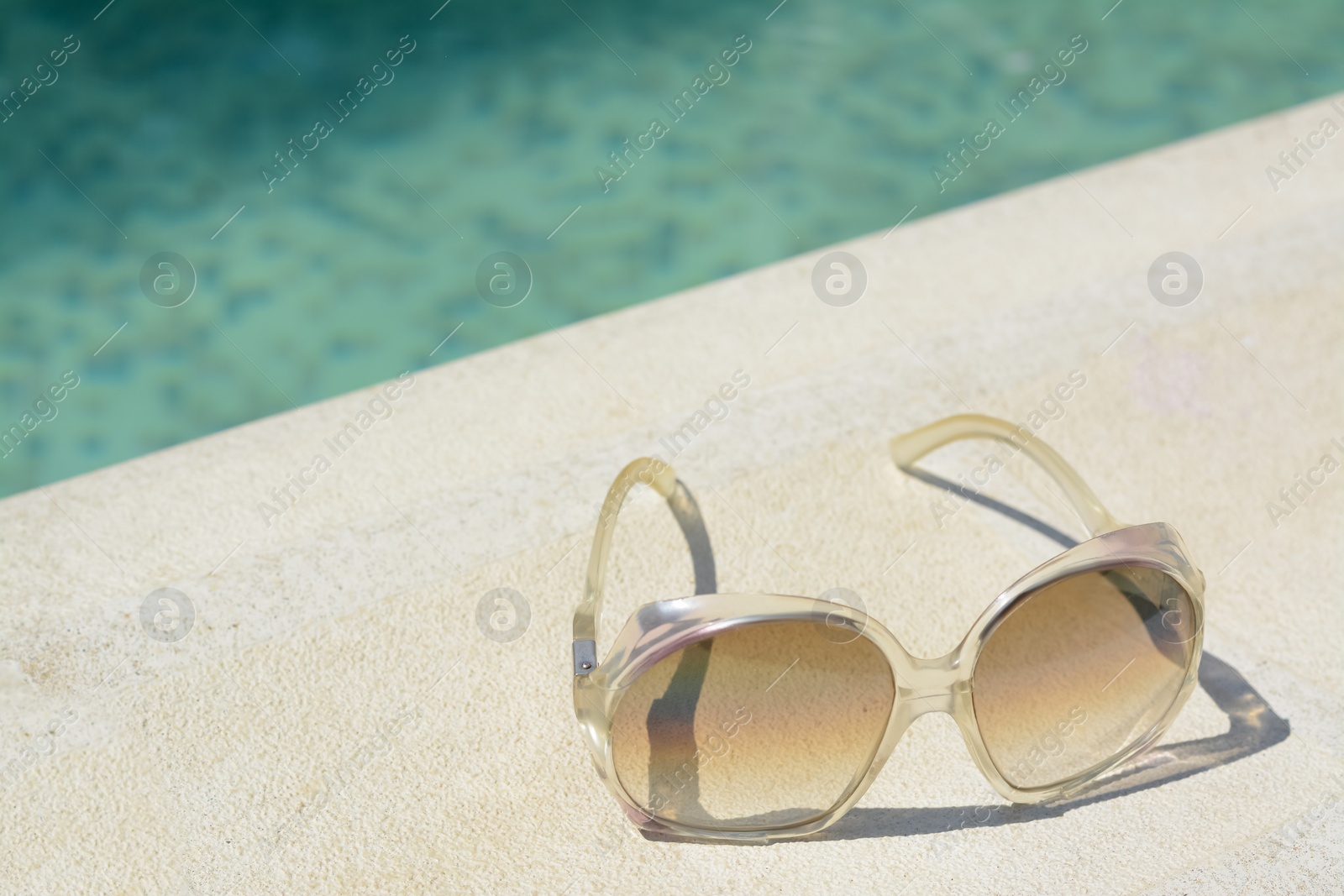 Photo of Stylish sunglasses near outdoor swimming pool on sunny day, space for text. Beach accessory