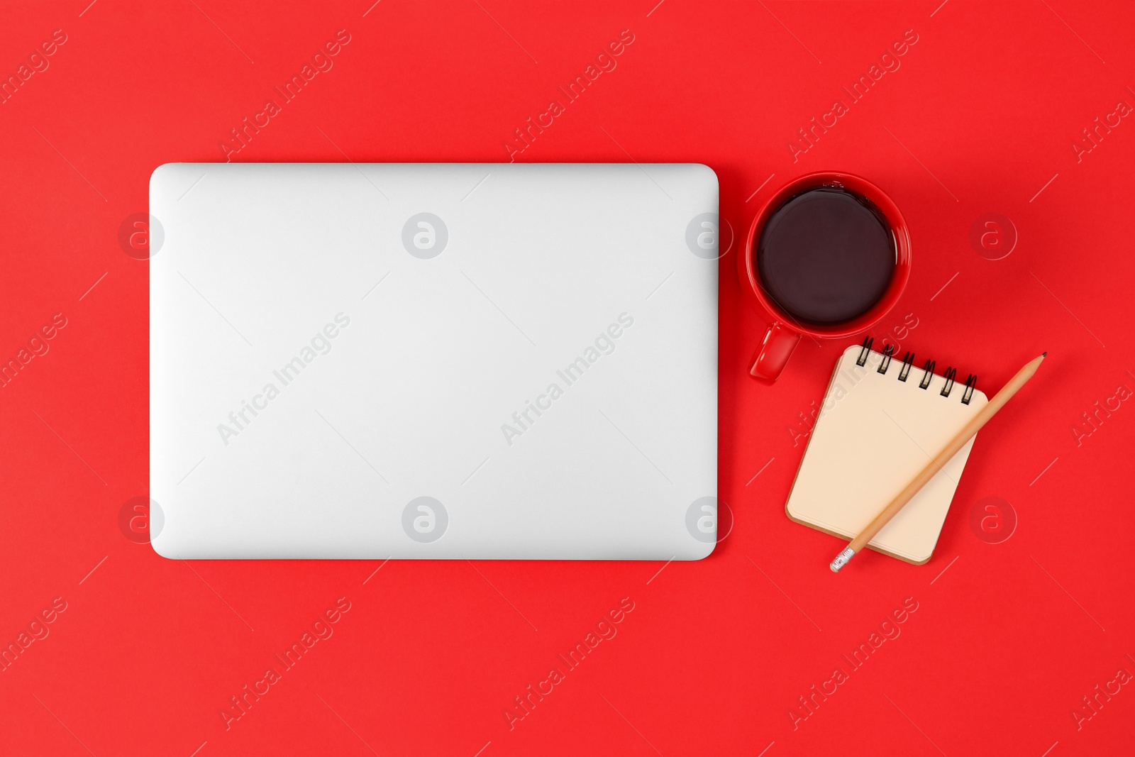 Photo of Modern laptop with cup of coffee and office tools on red background, top view