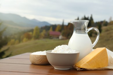 Photo of Tasty cottage cheese and other fresh dairy products on wooden table in mountains