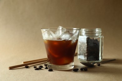 Photo of Refreshing iced coffee in glass, beans and straws on beige background, closeup